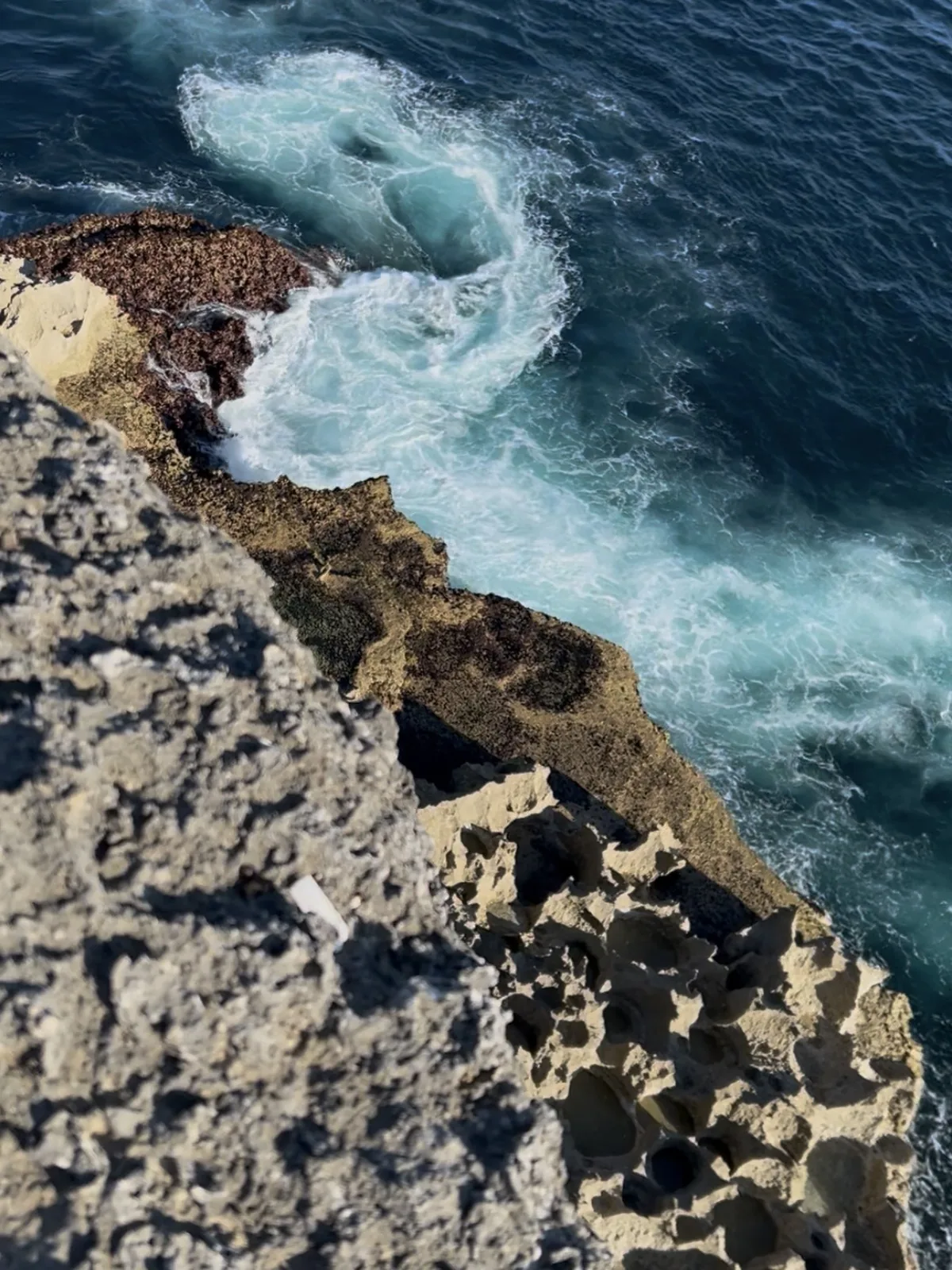 Plunging view of the Kelingking cliff at Nusa Penida, the turquoise ocean and the foam of the waves at the foot of the limestone rock